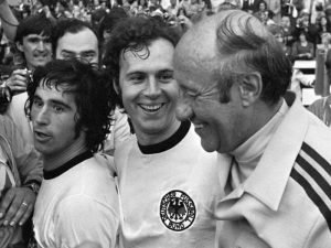 Franz Beckenbauer (Bildmitte) nach dem Gewinn des WM-Titels 1974 mit Gerd Müller (links) und Bundestrainer Helmut Schön. Foto: Wikipedia