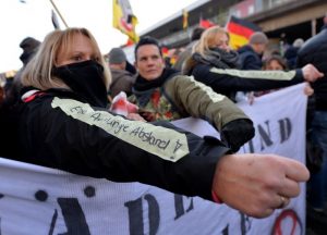 Auf dem Arm einer vermummten Teilnehmer der Demonstration von Pegida ist der Schriftzug "Eine Armlänge Abstand!" aufgeklebt. Foto: dpa